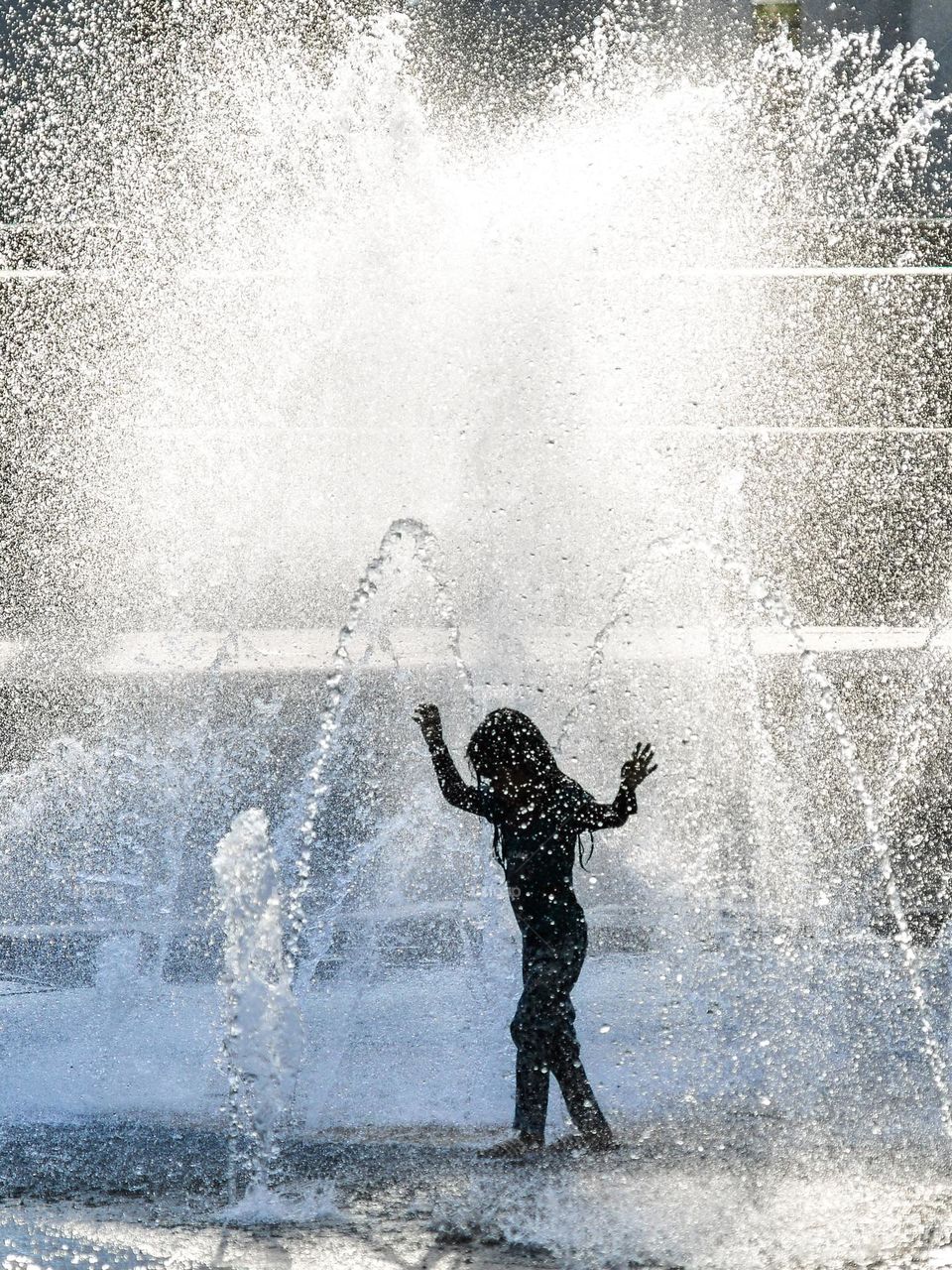 A silhouette of a girl playing in the city fountain to beat the heatwave