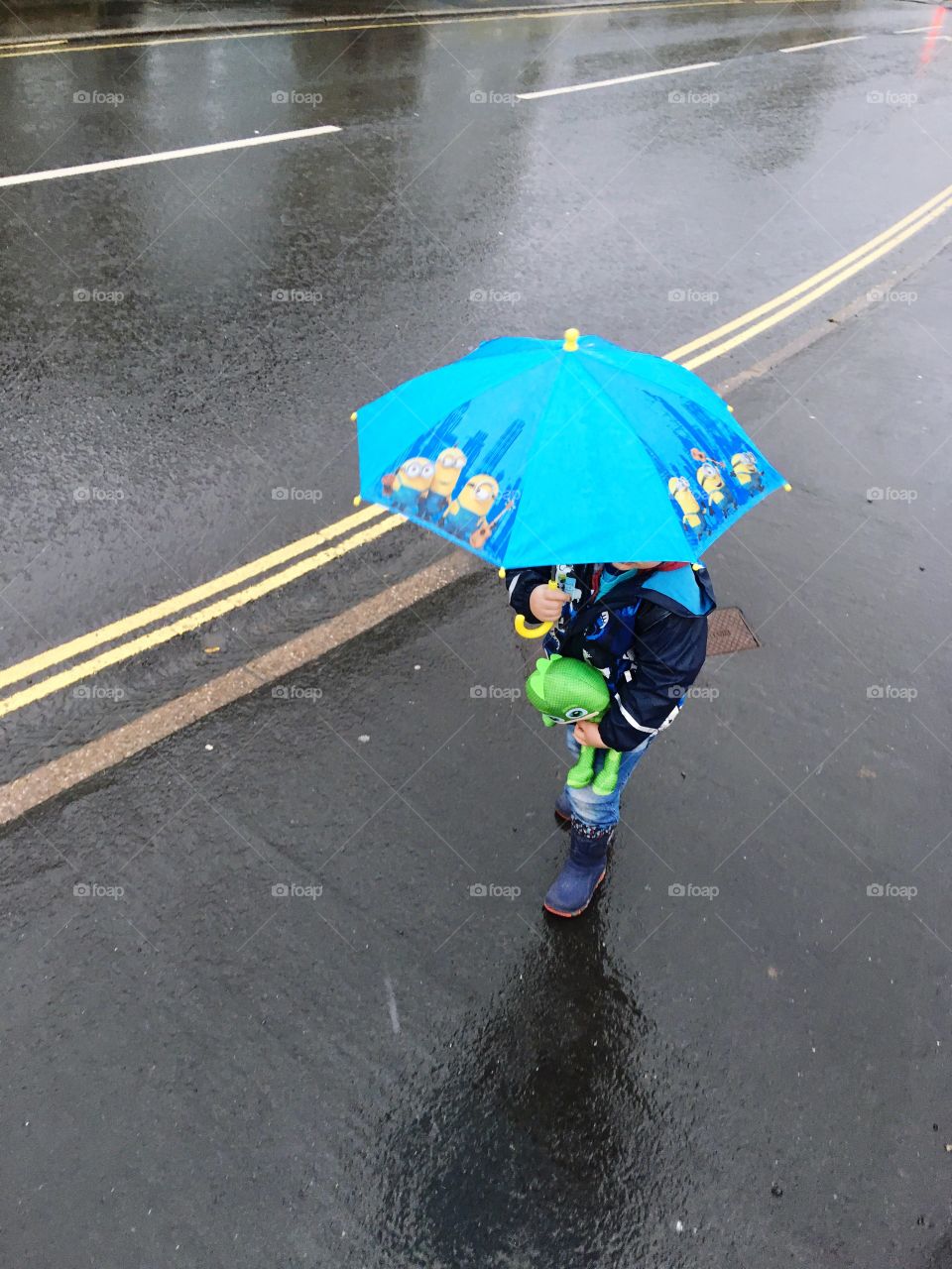 Child under minions umbrella, walking in the rain on a wet tarmac road in Ilfracombe North Devon