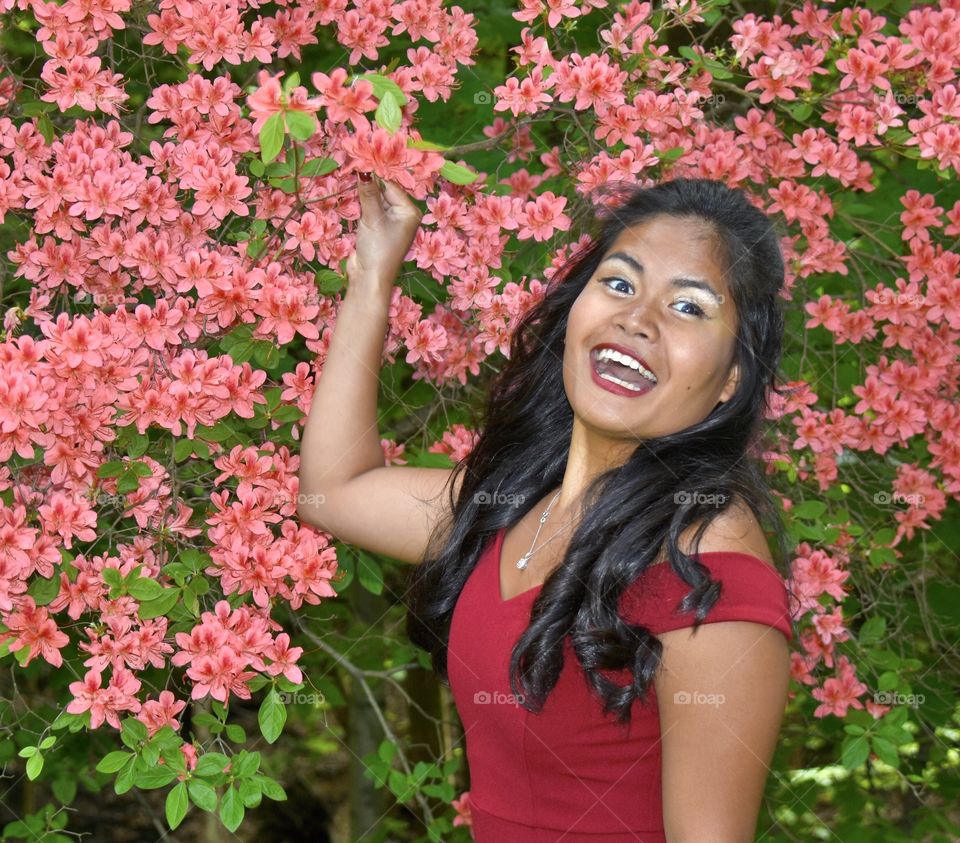 Girl acting silly, big smile, all dressed up standing in front of a flowering bush