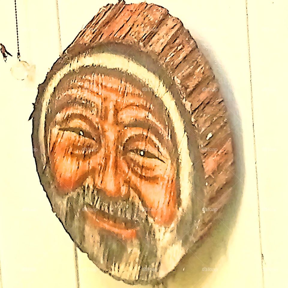 A smiling, kind faced, Inuit man, painted on a round, piece of wooden log making a beautiful hanging patio decoration.