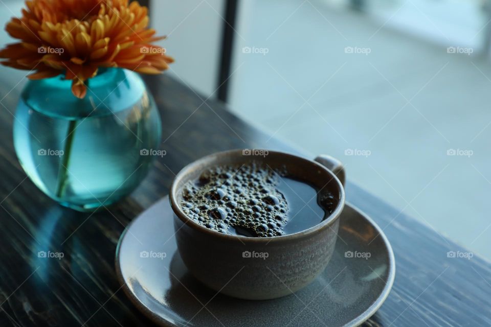 Cup of coffee and vase with flower on tabletop 