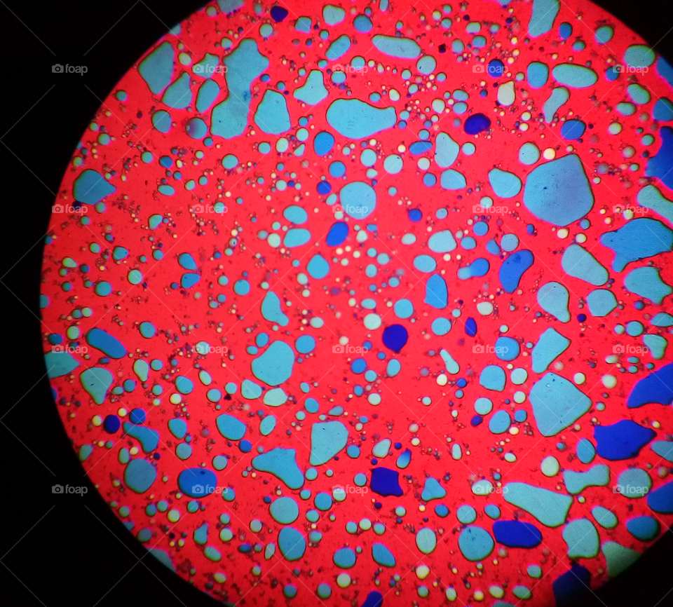 Microscopic red view of an emulsion with irregular mosaical blue shapes.