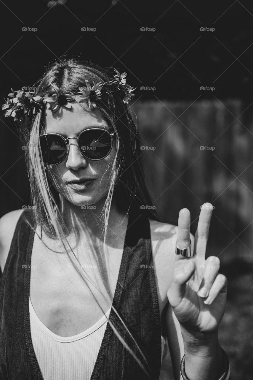 Black and white retro vibe image of a young woman wearing a flower crown and giving a peace sign on a sunny summer day 