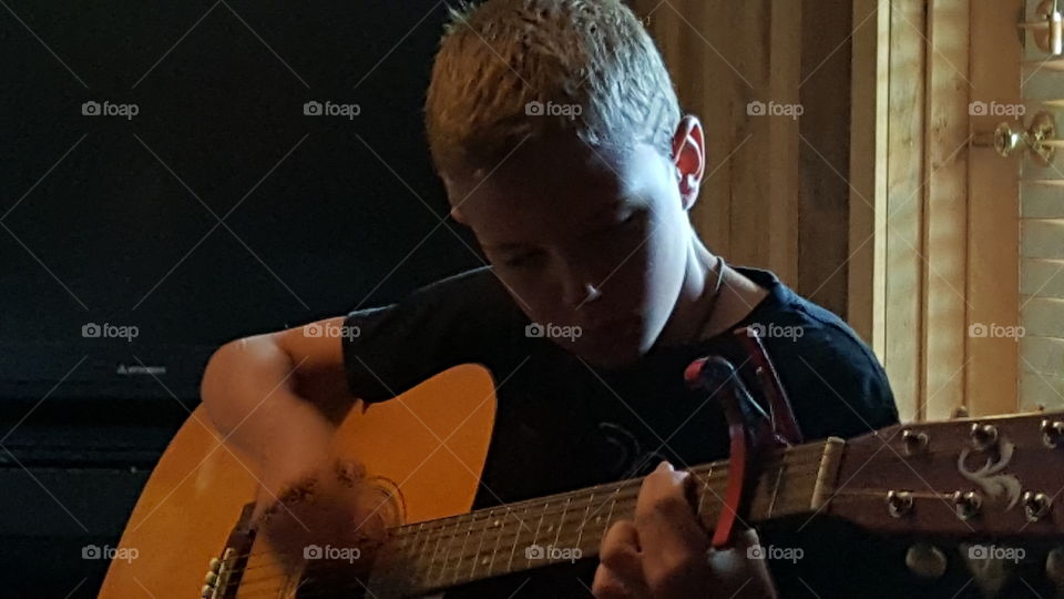 boy playing guitar working hard at perfecting his music