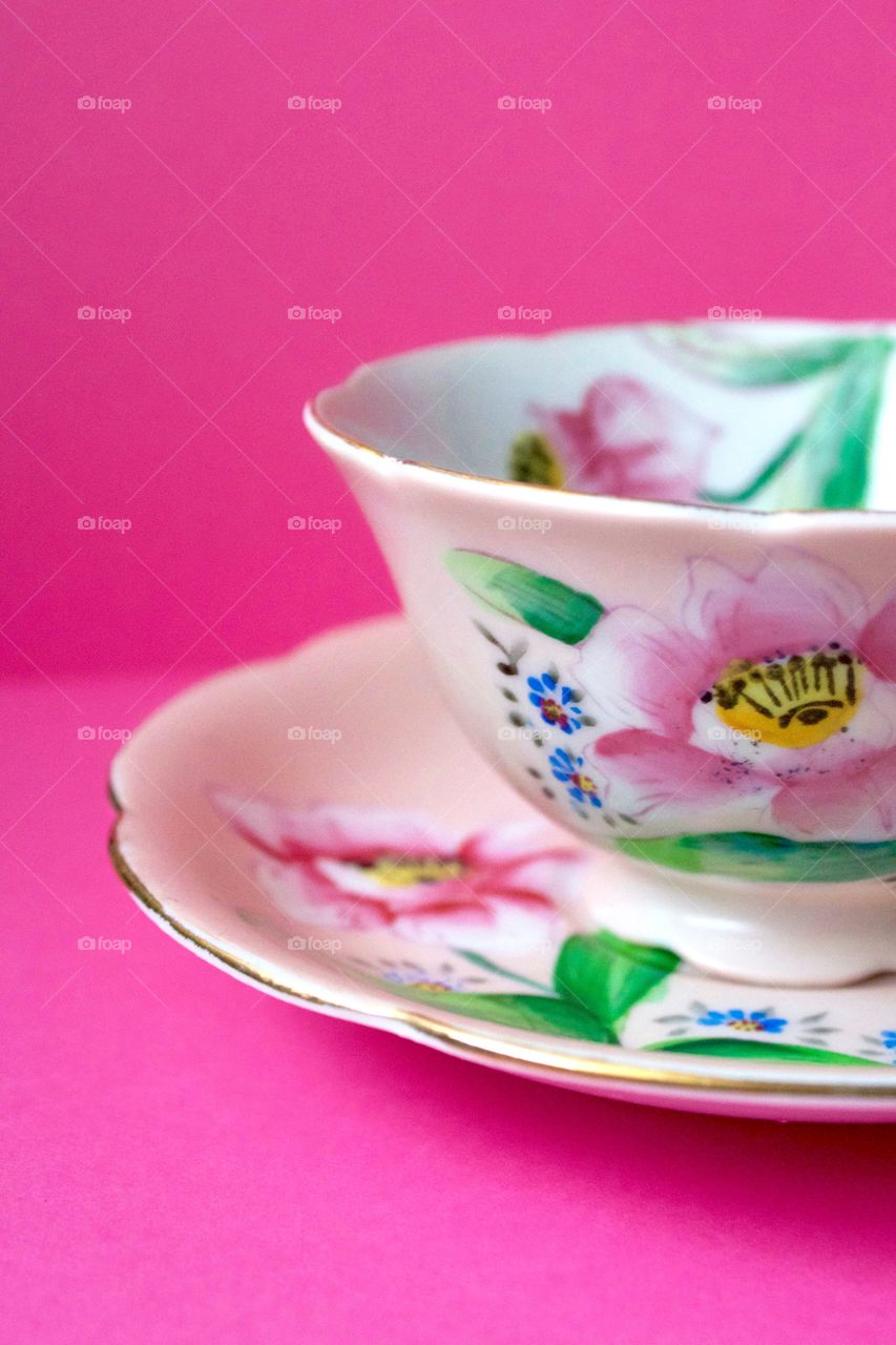 Color Love - Closeup of an antique hand-painted pink floral teacup on a bright pink background 