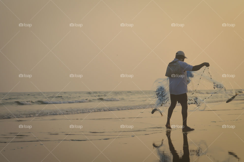 Fisherman catching fish with his fishing net in evening time in the beach of Indian Ocean The traditional way of fishing of coastal Indian people.