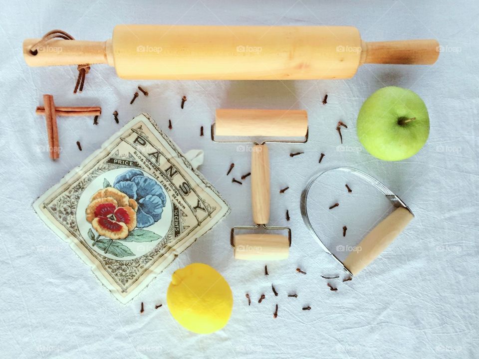 Thinking About Apple Pie - arranged flat lay of wooden kitchen utensils, a seed packet-themed potholder, green apple, lemon, cloves and cinnamon sticks on a flour sack kitchen towel, all ready for baking an apple pie 