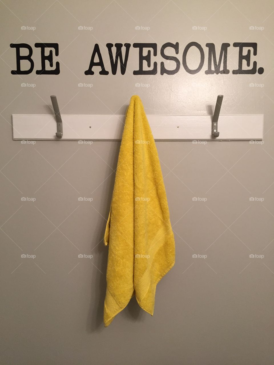 Be Awesome written on bathroom wall above bright yellow towel. 