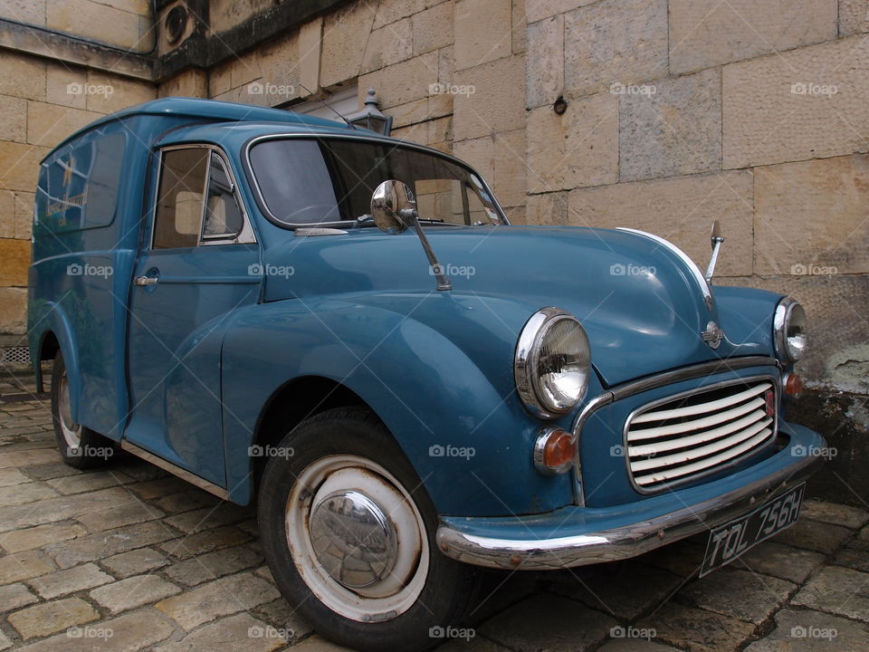 A vintage blue delivery car parked on stone on the exterior of Howard’s Castle outside of York in England on a summer day. 