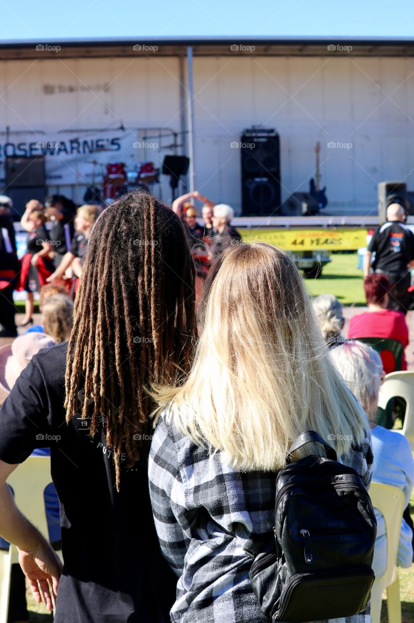 Long haired couple: man in brown dreadlocks, woman long blond hair back of head shots outdoor music festival 