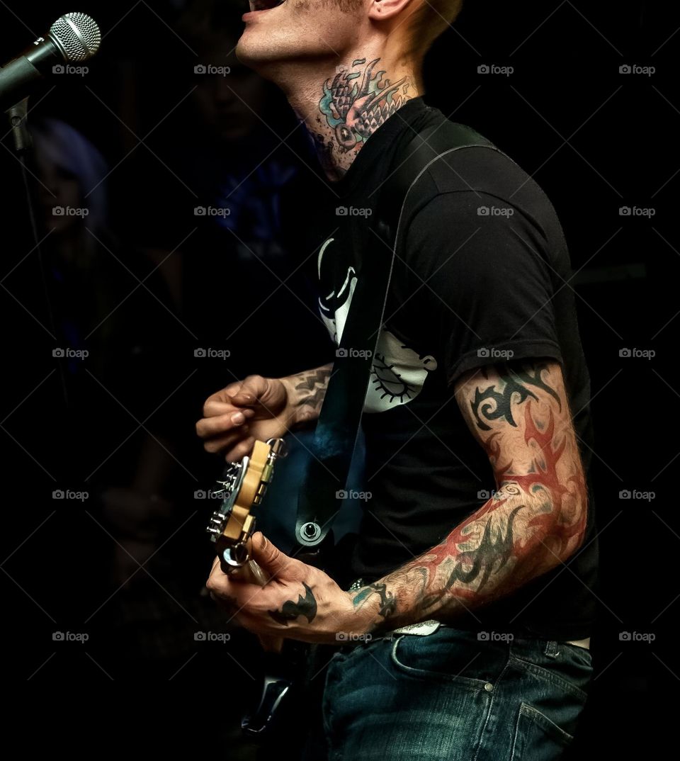 Man with tattooed neck & arms plays guitar