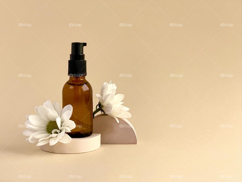 Glass bottle, white flowers, concrete props on beige 
