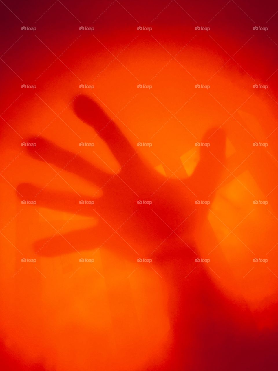My hand pressed on a orange balloon in front of a window whilst daylight floods the room