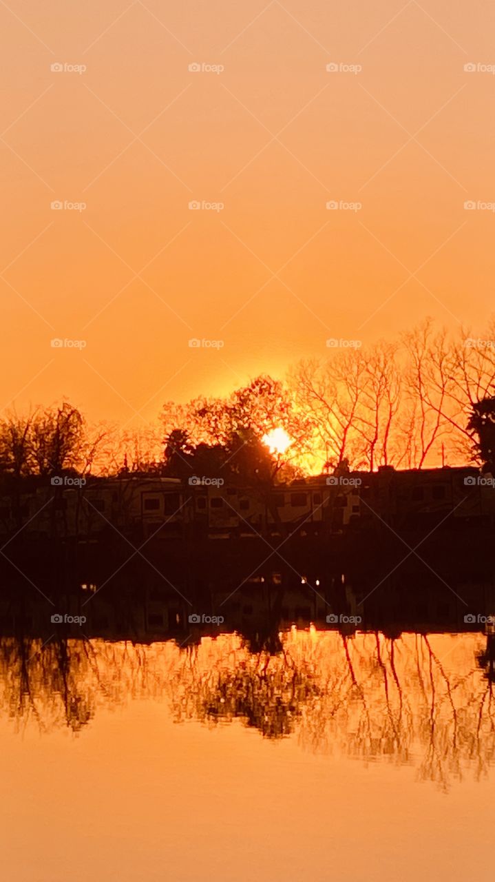Completely Slick Lake Waters. Sunset Colors in the Backlit Sky. Photographer using Elements of Landscape to paint his Picture. Captivating Gorgeous Beautiful Orange Glow Total Reflections from Landscape to Slick No Ripple Lake Waters.