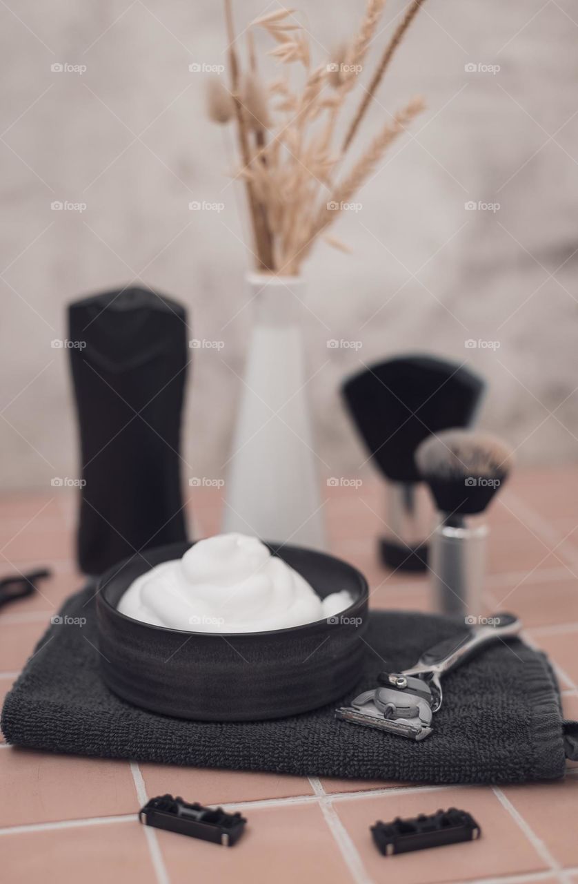 Shaving foam bowl,razor,shaving brushes,aftershave cream bottle,razor heads and ceramic vase with dried flower on brick natural tiled background,closeup side view plan with depth of field. The concept of a man barbershop, man shaving, beard care.