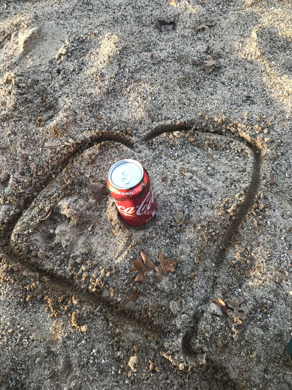 Coca Cola can with a heart drawn in the sand 