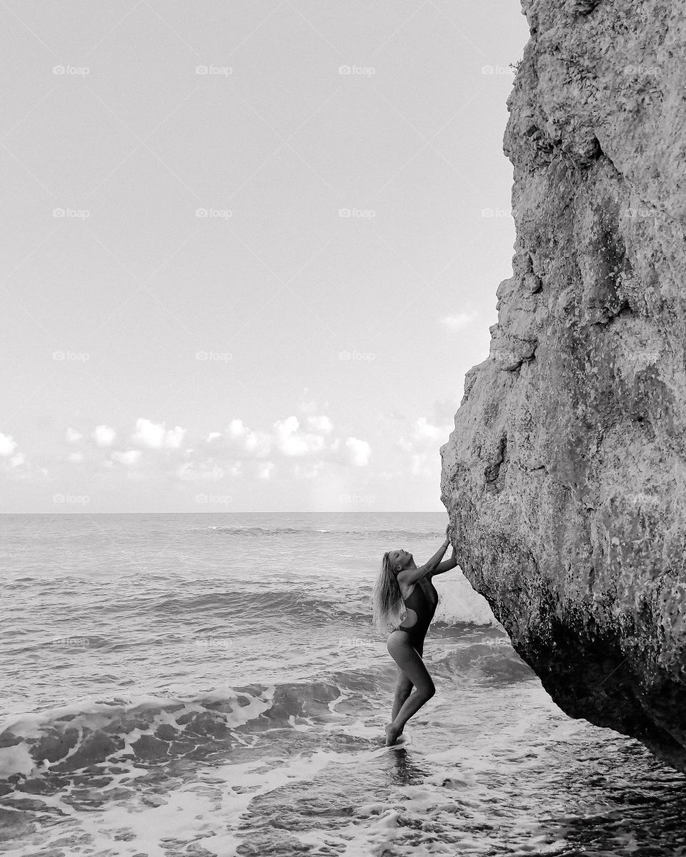 Black and white photo. Beautiful girl in a swimsuit in the sea at the cliff.