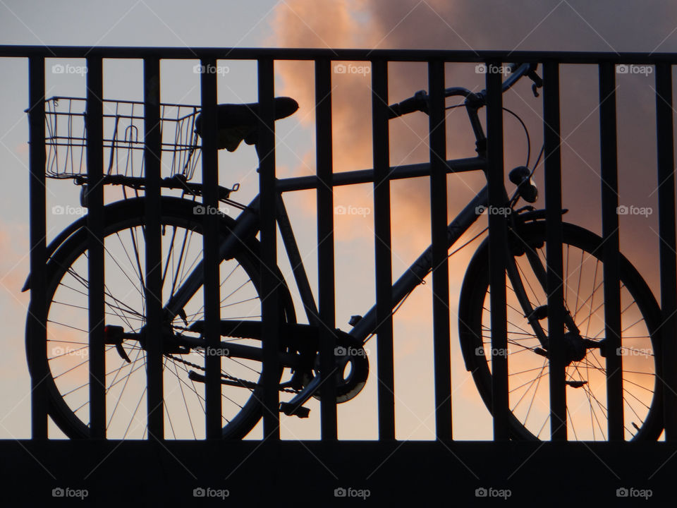 Silhouette of bicycle leaning on fence at sunset