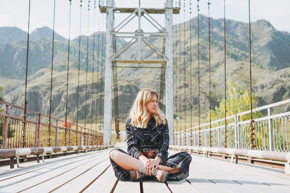 Happy young blonde woman in plaid dress on Horochowski bridge on Katun river, Altai mountains