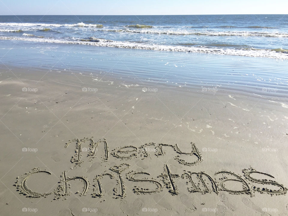 Merry Christmas written in the sand on the beach.