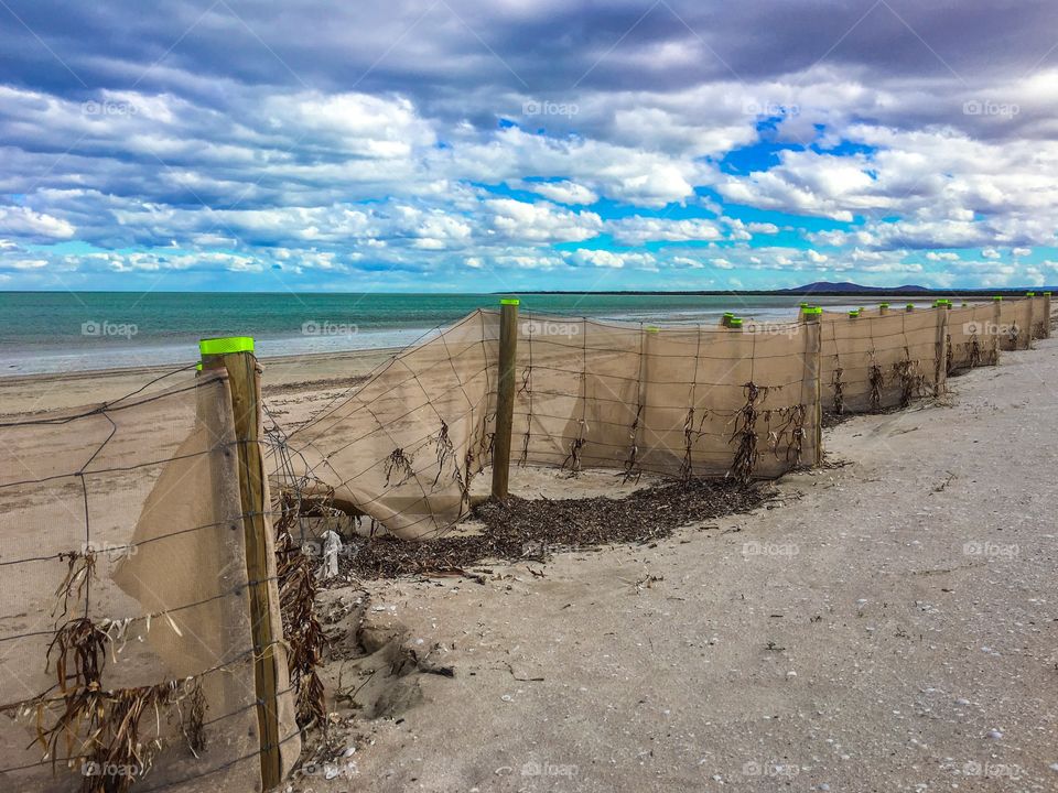 Perspective image long sand barrier fence on long stretch of beach on windy day in south Australia 