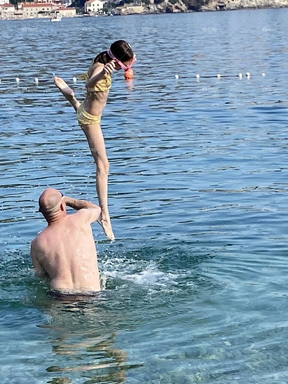 Girl in yellow bathing suit being thrown in the water by her dad.