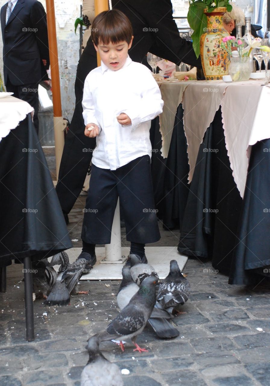 Feathered friends. A little boy feeds pigeons during a formal reception outdoors in Rome
