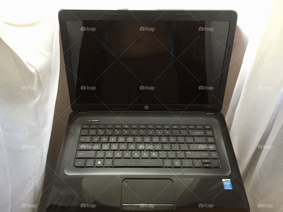 Hey black laptop computer in front of a window with white sheer curtains