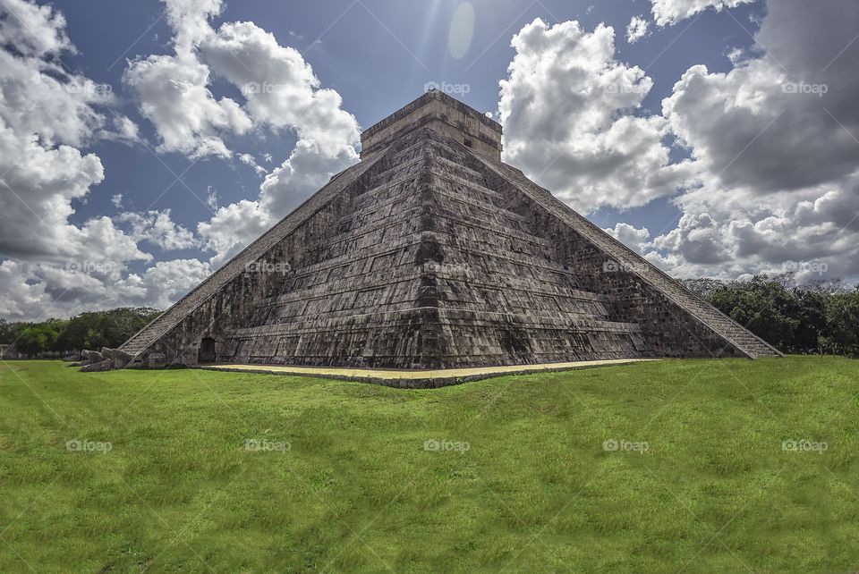 Panorama with the Pyramid of the archaeological complex of Chichen Itza in Mexico surrounded by natural vegetation under a sky with sheepish clouds and some tourists who admire it ecstatic.