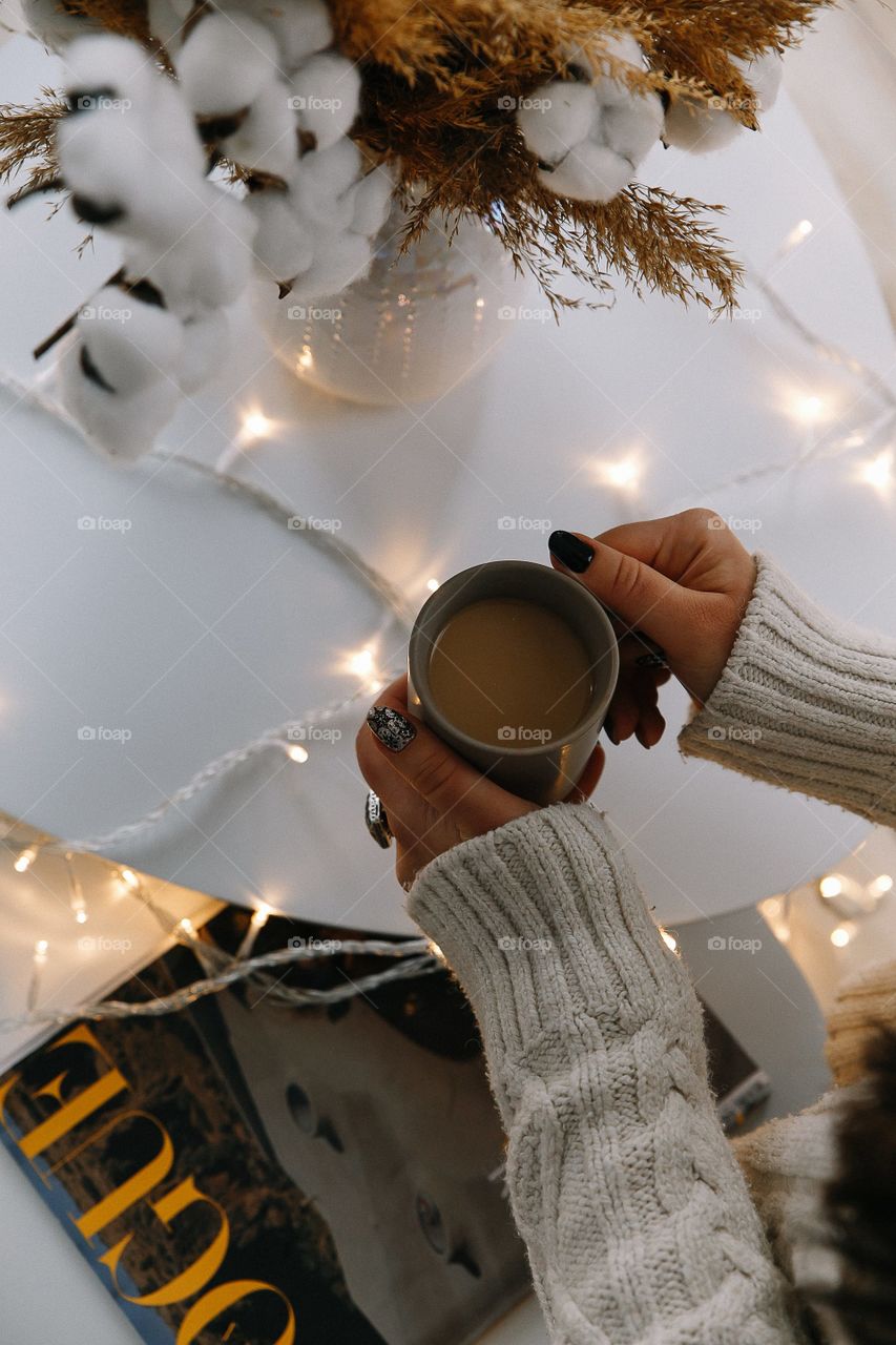 Cup of coffee with milk in female hands on white table