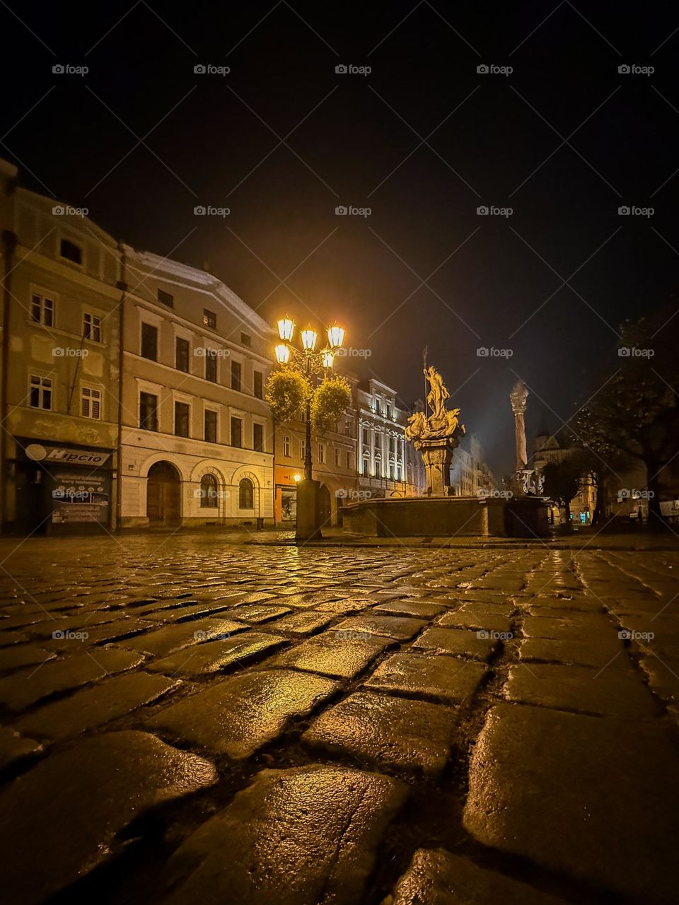 Empty foggy street in Poland after the rain, paving stones, old architecture, ancient fountain and warm light