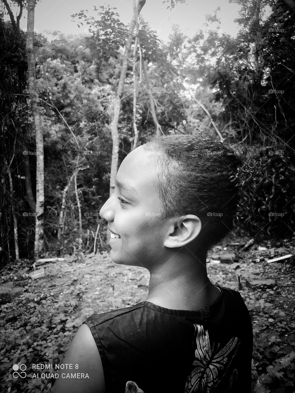 Edição em preto e branco destacando o sorriso e a beleza do rosto da modelo em uma chácara com muitas plantas renovando as folhas com a água da chuva