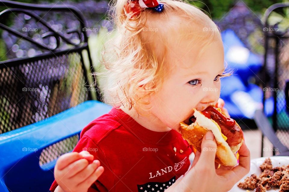 Hotdog!. Baby eating a hotdog with ketchup and mustard 