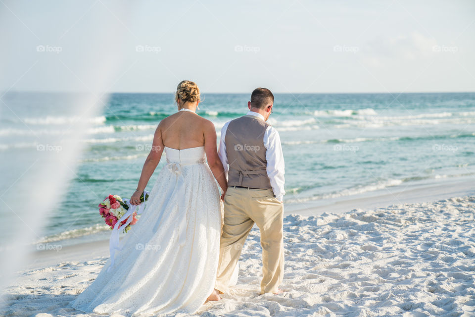 Bride and groom walking down the beach holding hands 