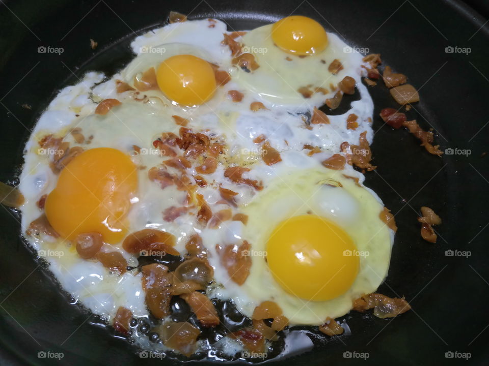 Uncooked fried eggs and bacon fat frying