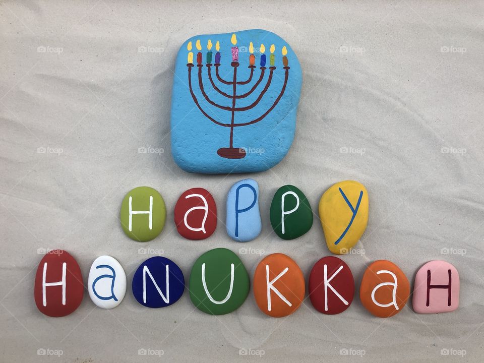 Happy Hanukkah, Jewish festival of lights with colored stones design over white sand