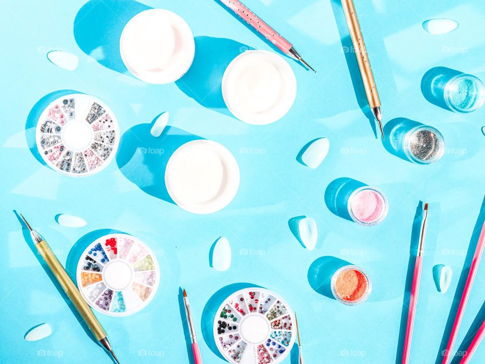 Set of nail bank with glitter,different brushes and artificial false plastic nails on blue background, flat lay. Concept cosmetics and beauty salons.