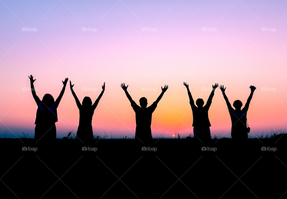 Silhouette of people raising hands up during sunset
