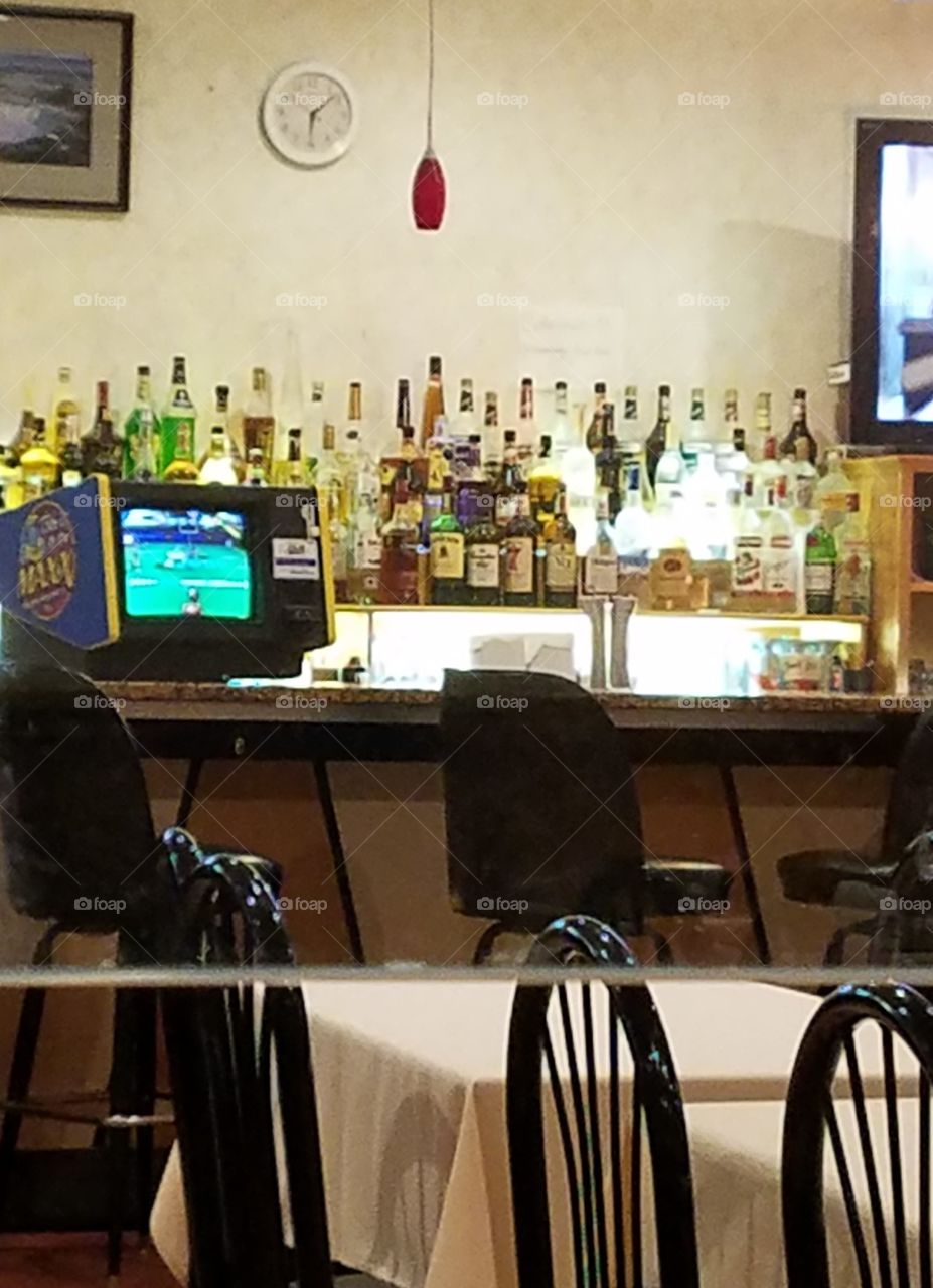 Bar with bottles, TV, stools, nobody there, early evening, restaurant empty too.