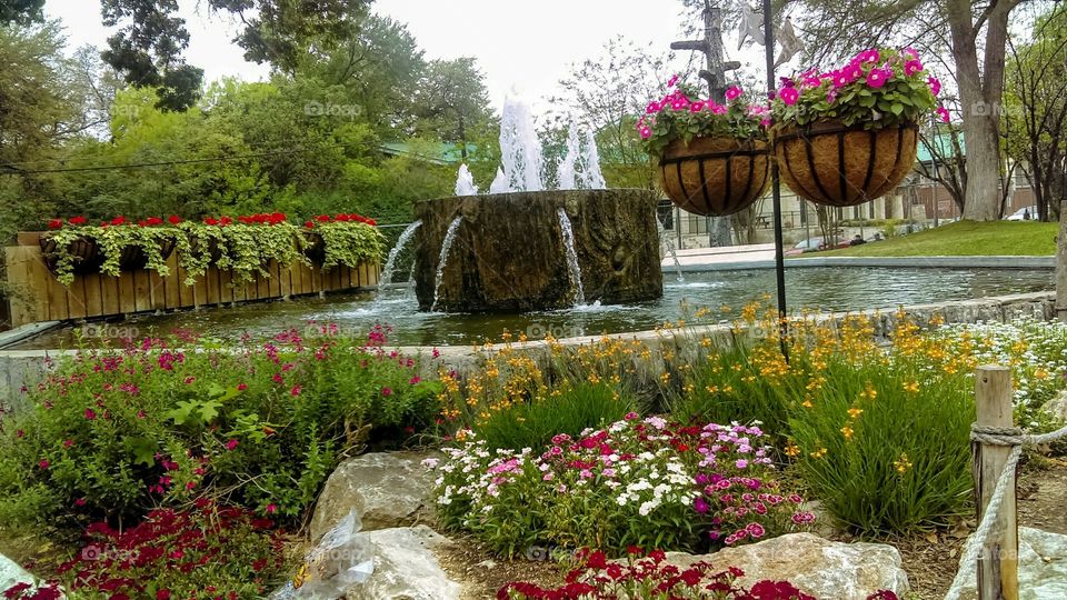 Beautiful landscaping water fountain additional by colorful flowers.