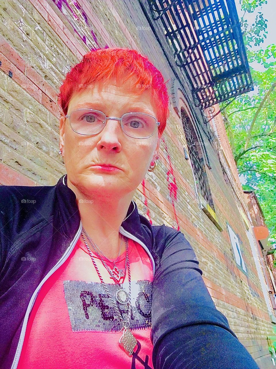 I, “Petra Schiller” wearing a pink sequined shirt inscribed with the words “PEACE” and “LOVE” and intensely bright red short hair am sitting on our favorite stoop on “Waverly Av” in “Clinton Hill”, Bklyn today. 2021. Hypnotic Productions