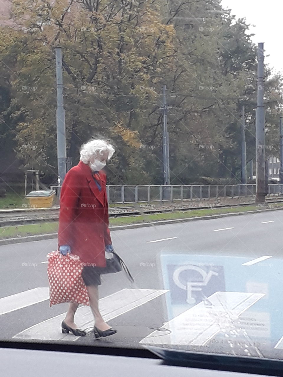 street trafic in 2020 - an eldery lady in mask crossing  street  as seen  through the windscreen