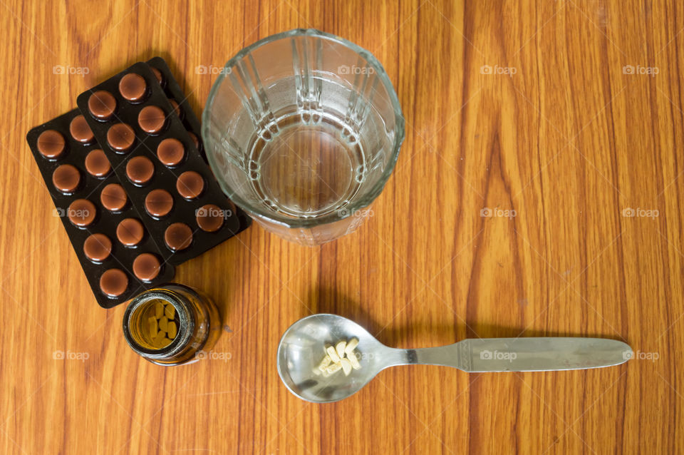 View of antioxidants vitamin tablet, pill blisters, a bottle of drug, capsule in measuring spoon, with glass of water placed on the table. Medical Pharmacy theme. Side view, Close up with copy space.