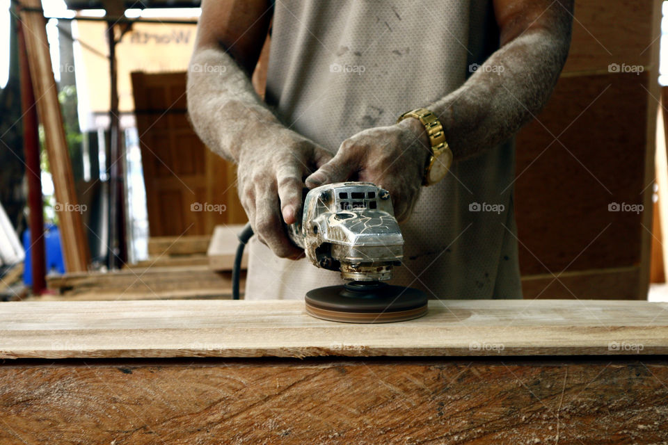 hand of a carpenter smoothing a plank of wood with a grinder