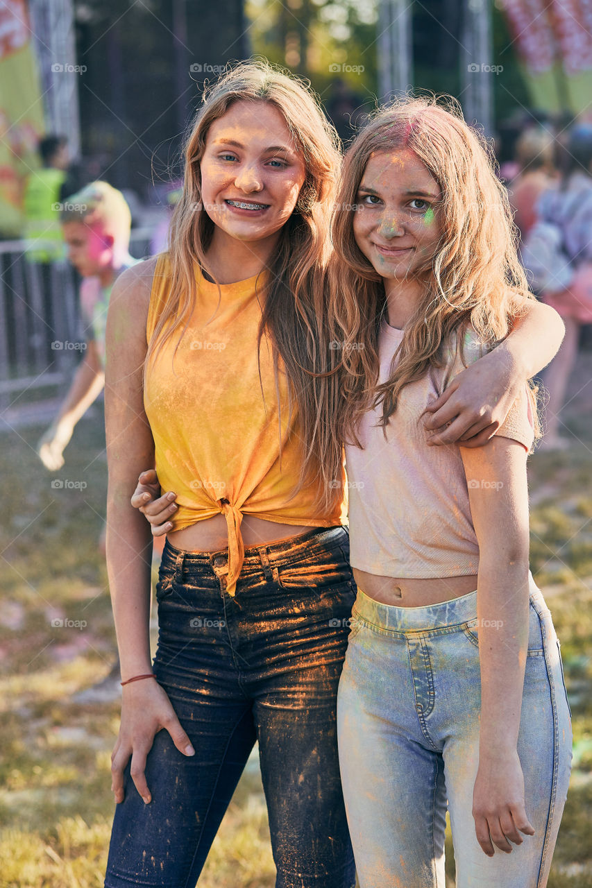 Portrait of happy smiling young girls with colorful paints on faces and clothes. Two friends spending time on holi color festival. Real people, authentic situations