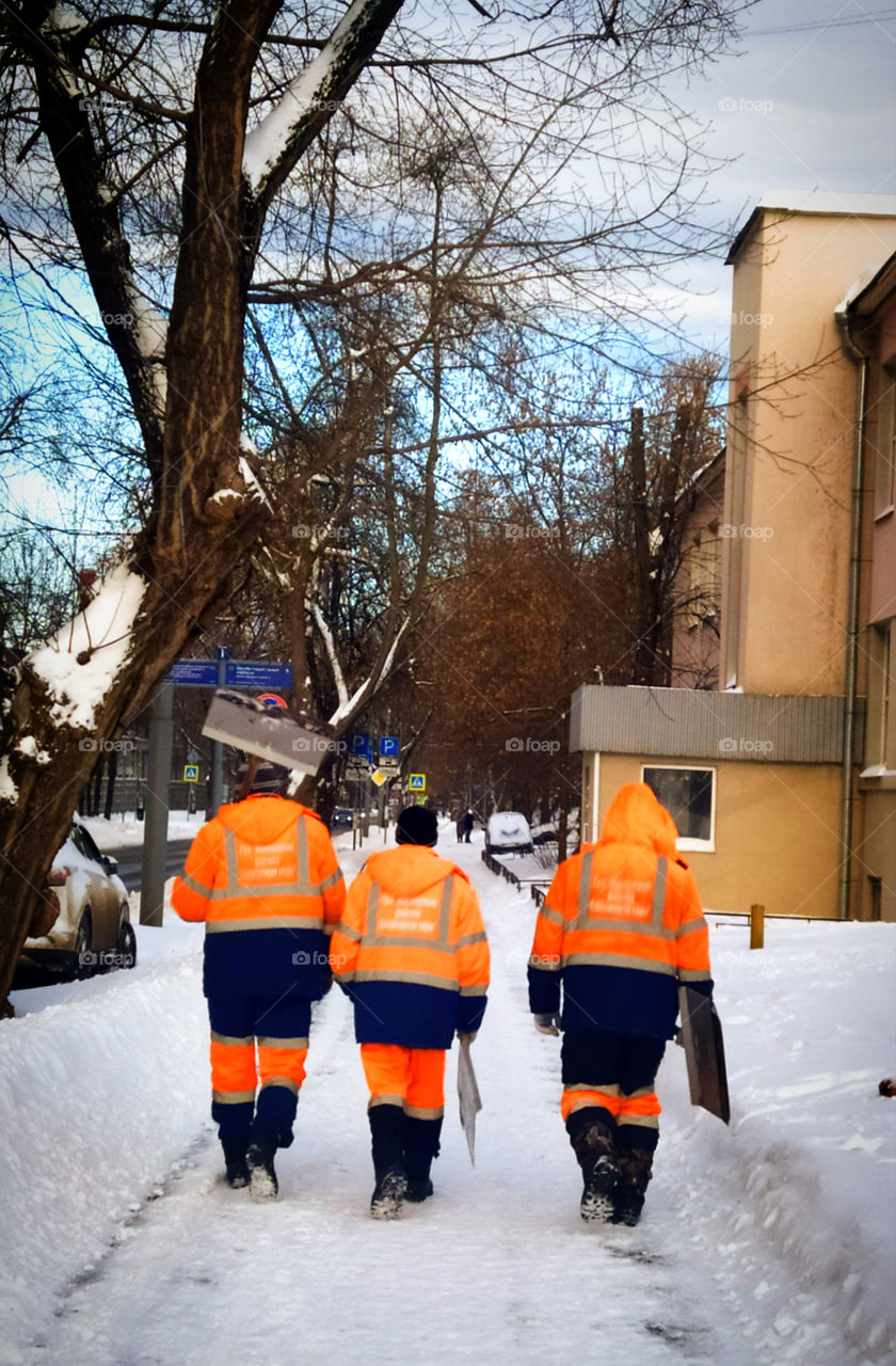 Three men in uniforms with metal shovels go to clear the snow