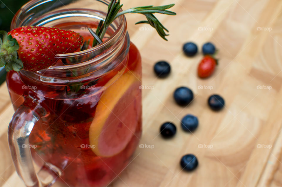 Elevated view of beautiful fresh berry flavored water in glass jar on wood with organic strawberry, blueberry, Rosemary and citrus sliced lemon lime for a homemade variation of gourmet berry lemonade 