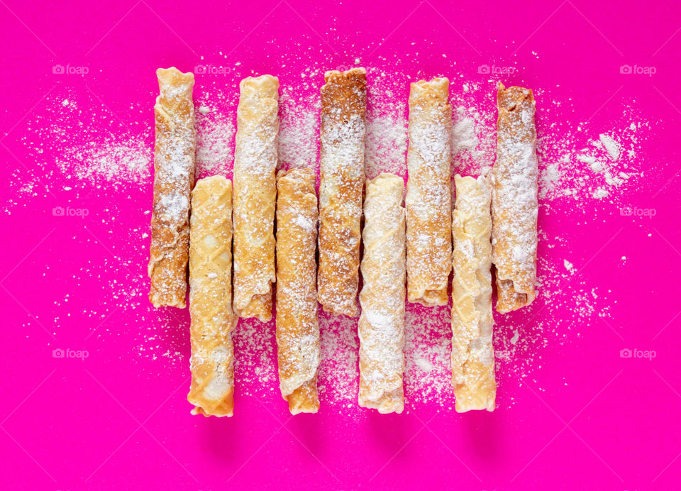 Homemade cake. Delicious waffle tubes with powdered sugar on a bright pink background. Delicious sweet snack, top view. Children's treat