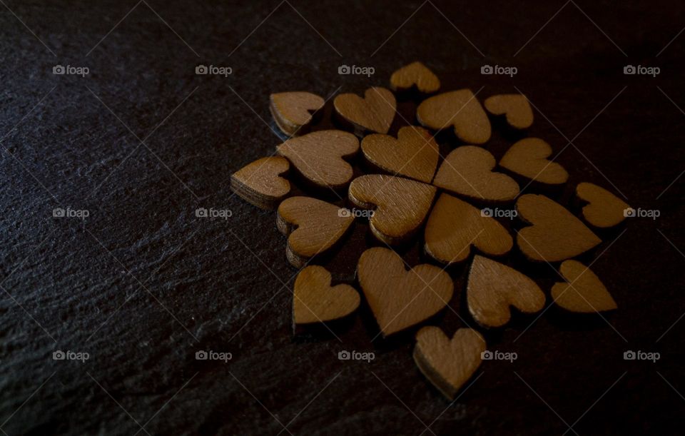 Small wooden hearts placed in a pattern on a dark wood background 