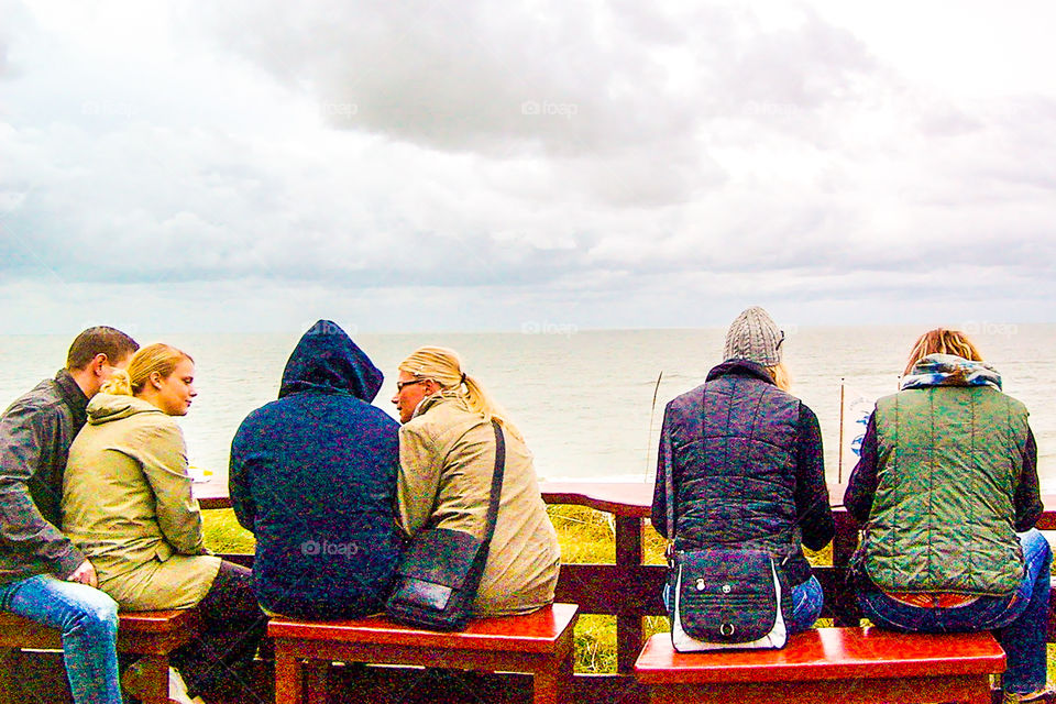 Junge Frauen und Männer sitzen an der Küste mit Blick auf das Meer und unterhalten sich